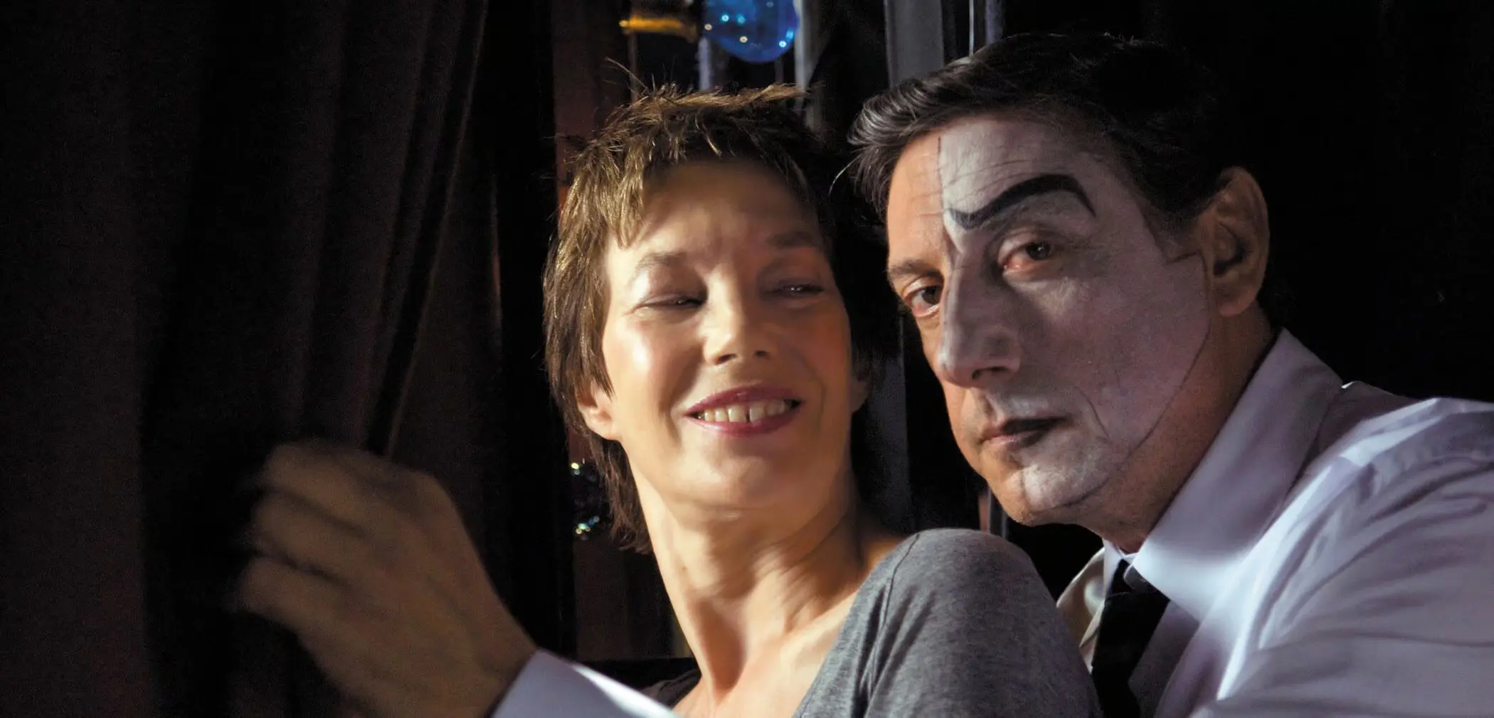 Two actors smiling in a dimly lit theatrical setting